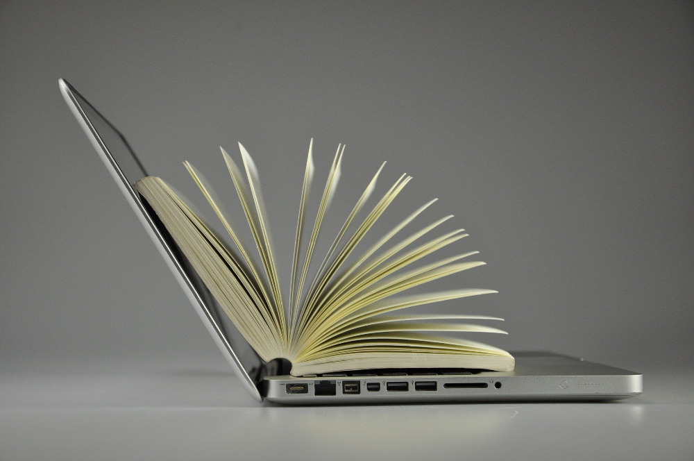 Open textbook resting on a laptop keyboard, symbolizing online learning, digital resources, and comprehensive study materials for personal training certification programs and fitness education.