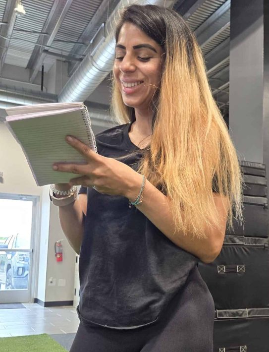 Female personal training student reviewing notes in a gym setting, representing the academic and practical learning balance in our fitness certification programs.